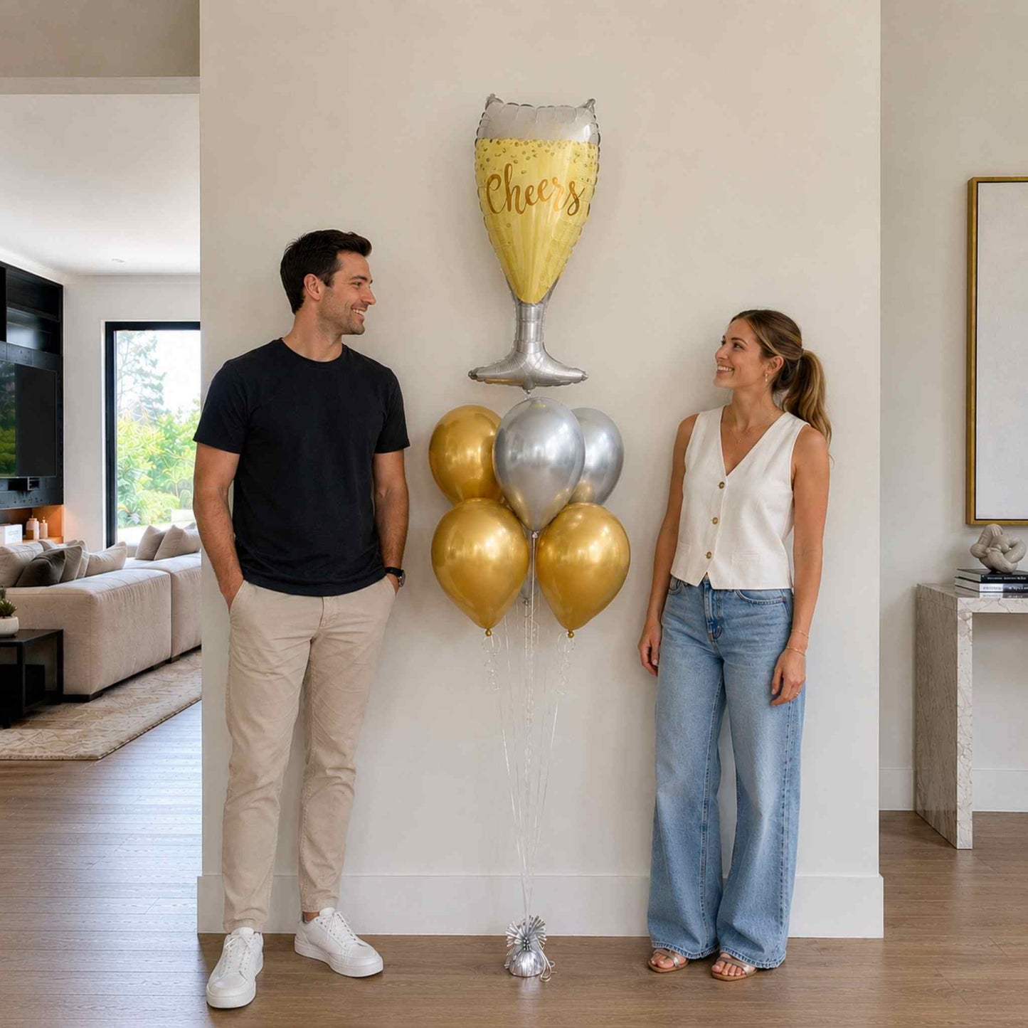 Man and woman standing in a living room with decorative balloons shaped like a champagne glass and balloons.