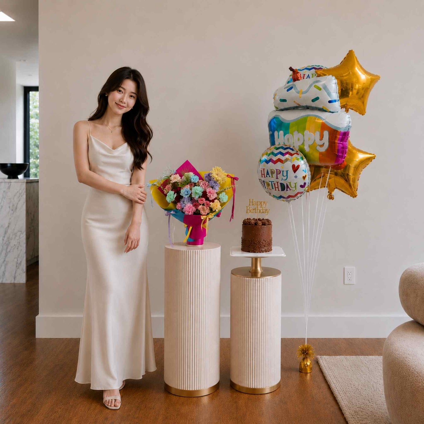 Woman in a white dress standing next to a cake and balloons in a room.