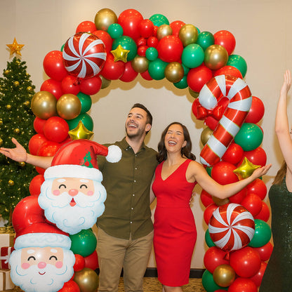 Two people posing in front of a festive balloon arch with Christmas decorations.
