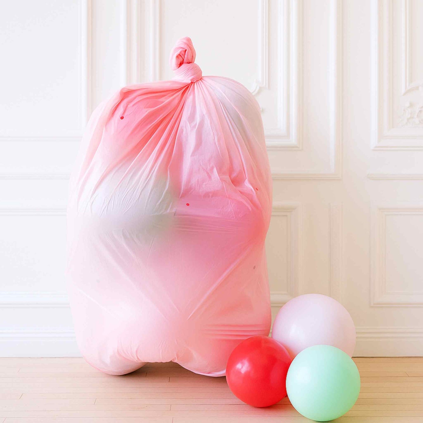 Pink trash bag with balloons on a wooden floor against a white wall