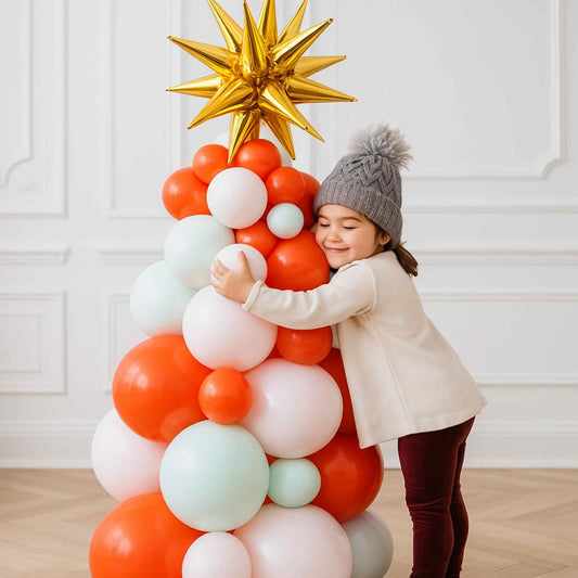 Child hugging a colorful balloon tree with a gold star on top against a white wall.