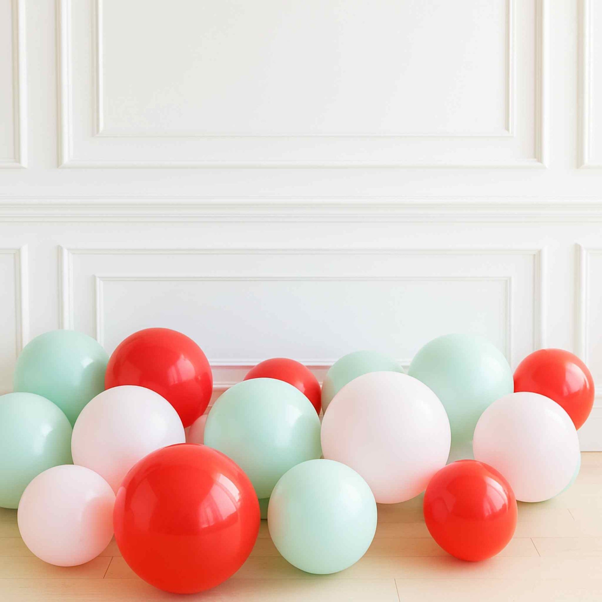 Colorful balloons in red, green, and white on a light wooden surface with a white paneled wall background.