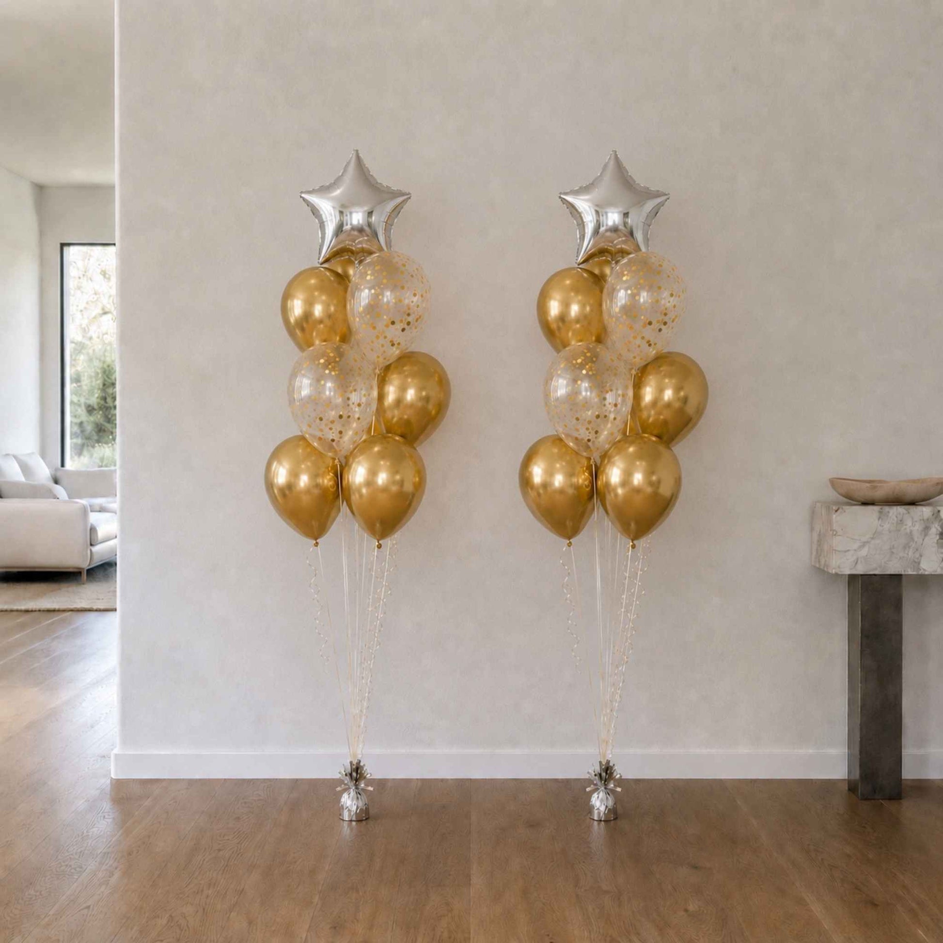 Two tall balloon arrangements with gold, silver, and clear balloons against a white wall.