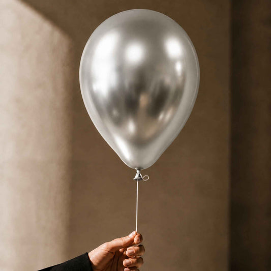 A metallic silver latex balloon held by a hand against a warm, textured beige wall.