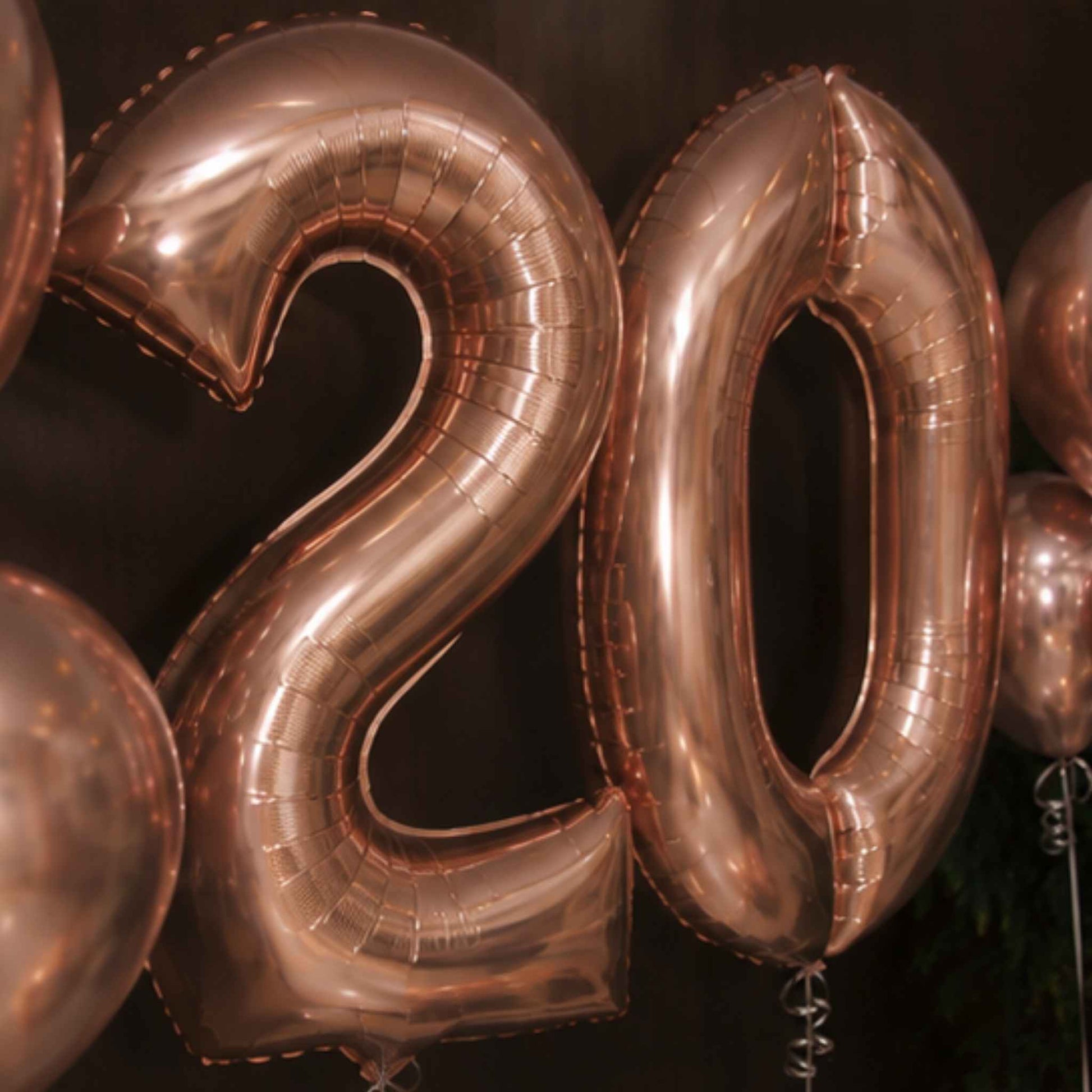 Rose gold foil balloons spelling out the number 20, photographed against a dark background.