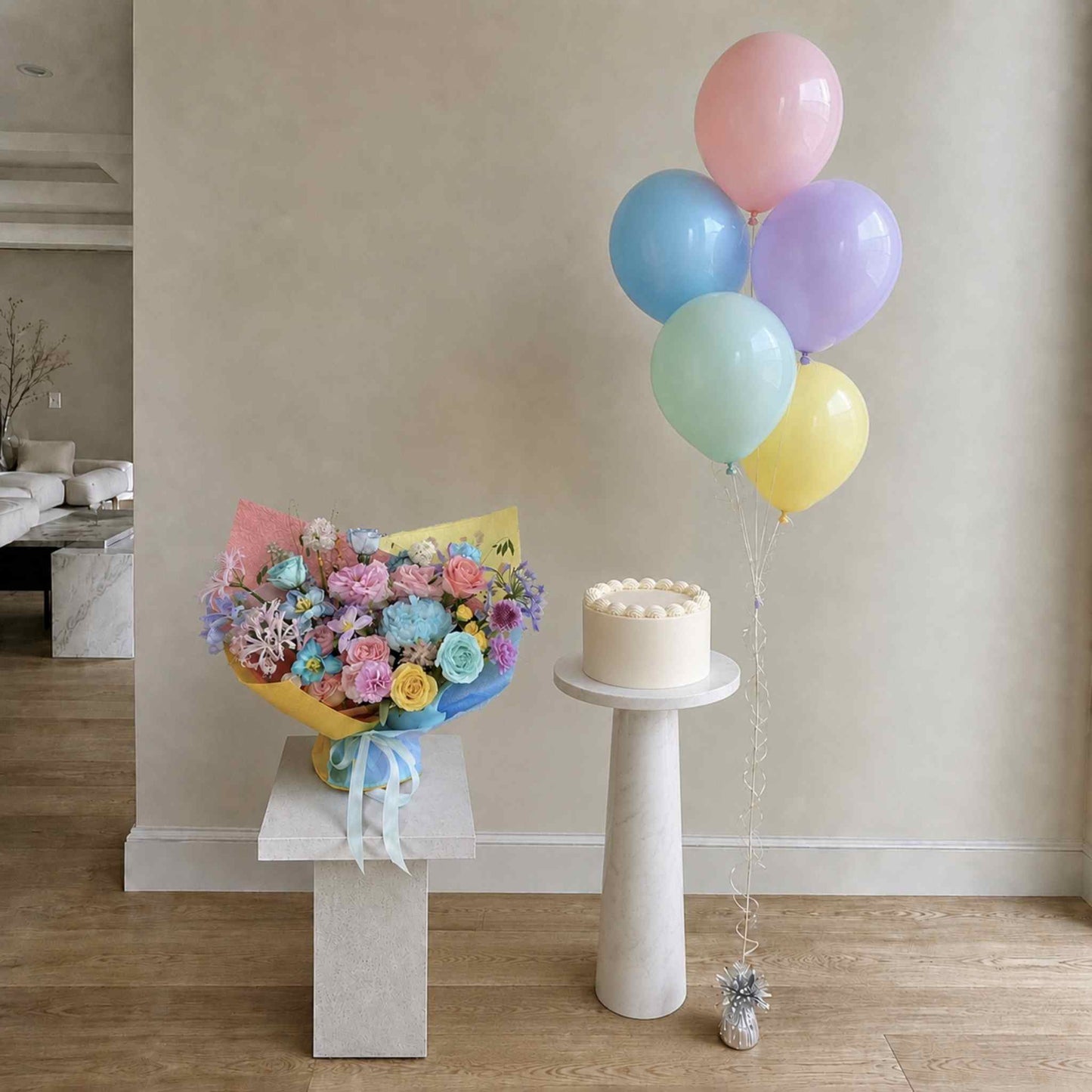 Bouquet of flowers and cake with pastel balloons on a table in a room.