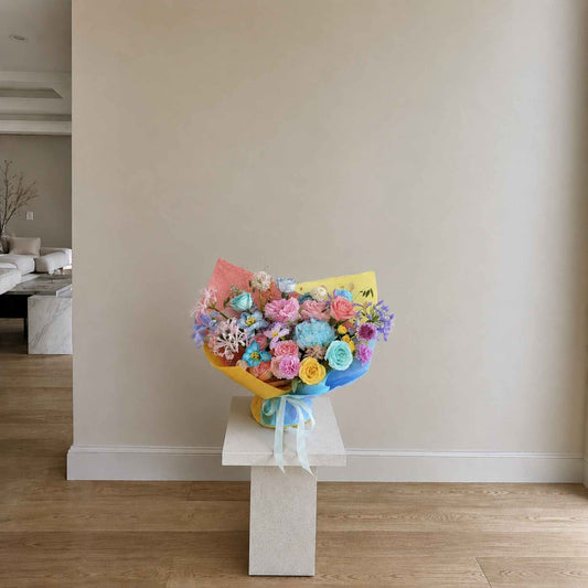 Colorful bouquet of flowers on a white pedestal against a neutral wall.