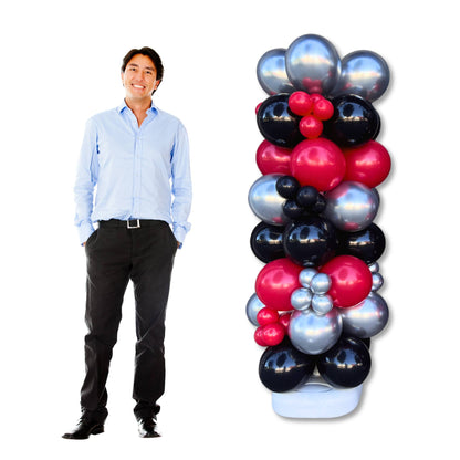 A person standing next to a 6ft tall balloon column decorated with a mix of blue, red, and silver balloons.