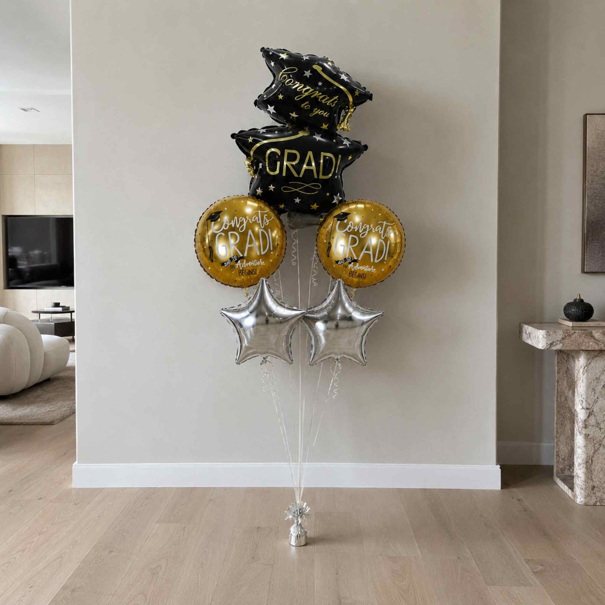 Graduation-themed balloons in black, gold, and silver in a living room setting.
