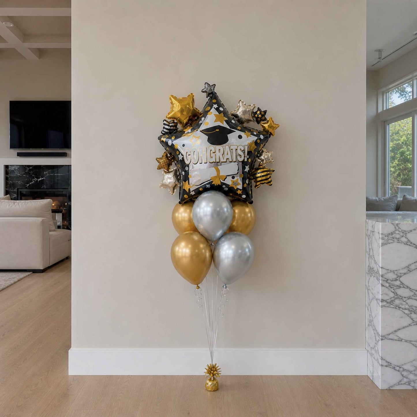 Graduation-themed balloon bouquet with gold, silver, and black balloons in a living room.