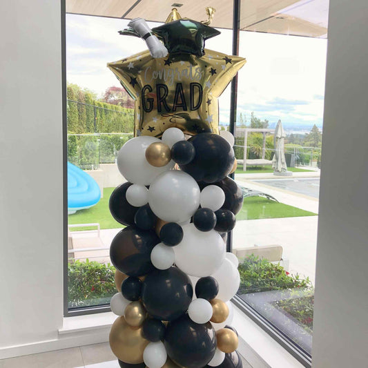 Graduation-themed balloon arrangement with a 'GRAD' balloon in front of a window.