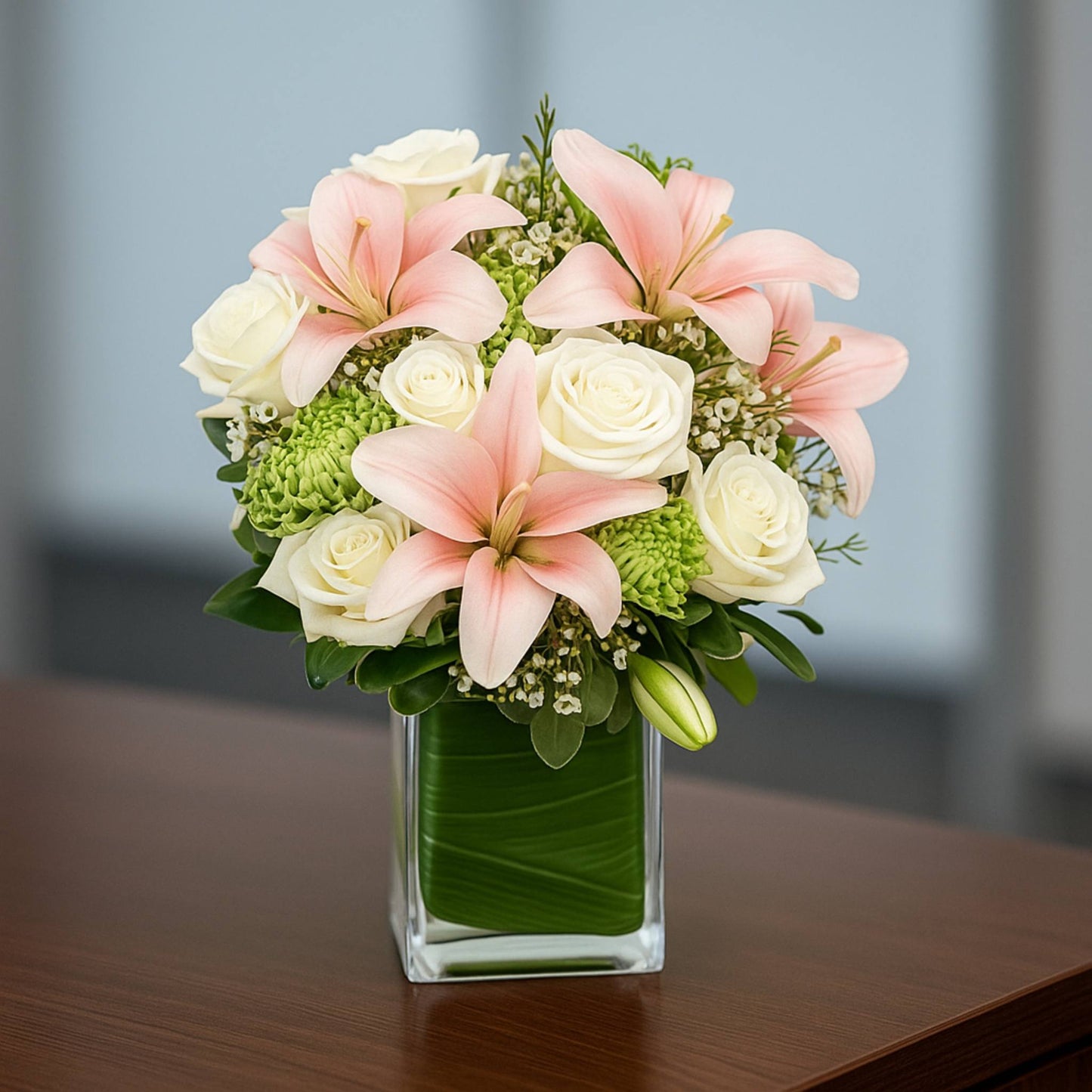 Bouquet of pink and white flowers in a clear vase on a wooden surface with a blurred background