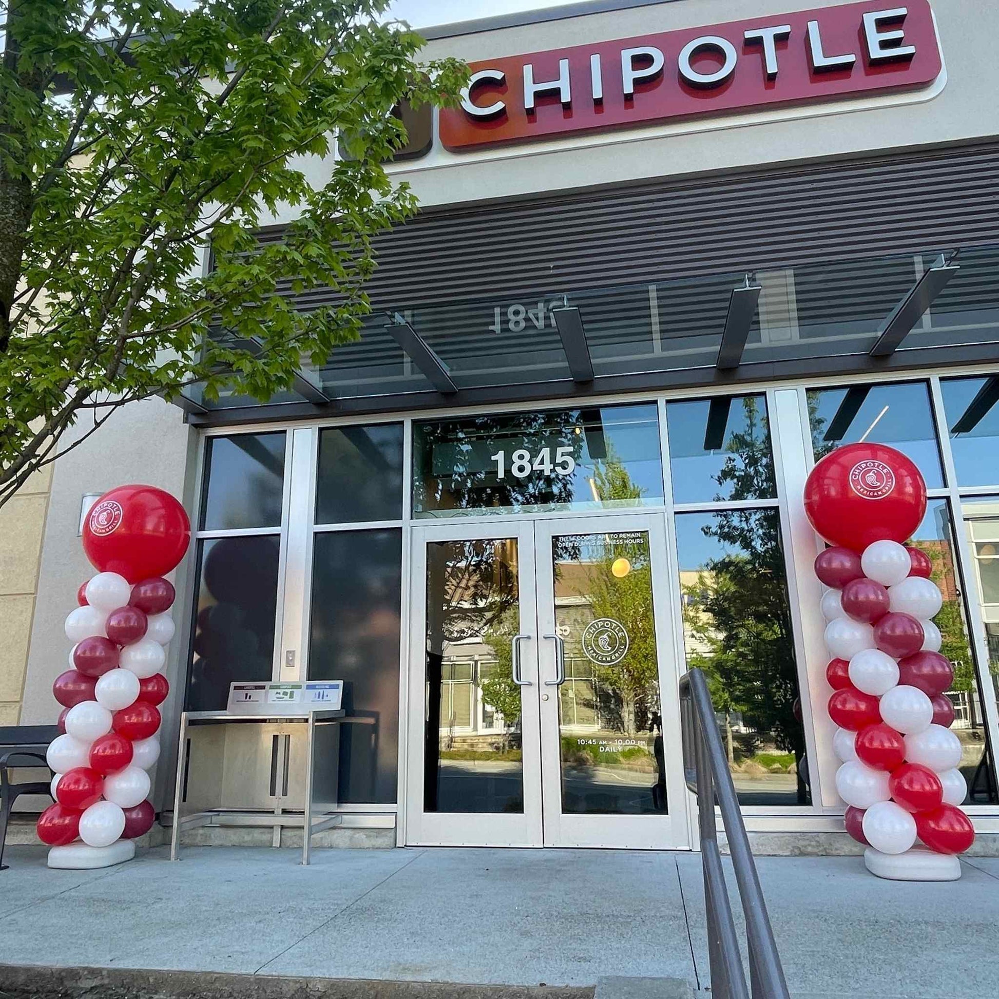 Chipotle restaurant entrance with red and white balloon arches on a clear day.