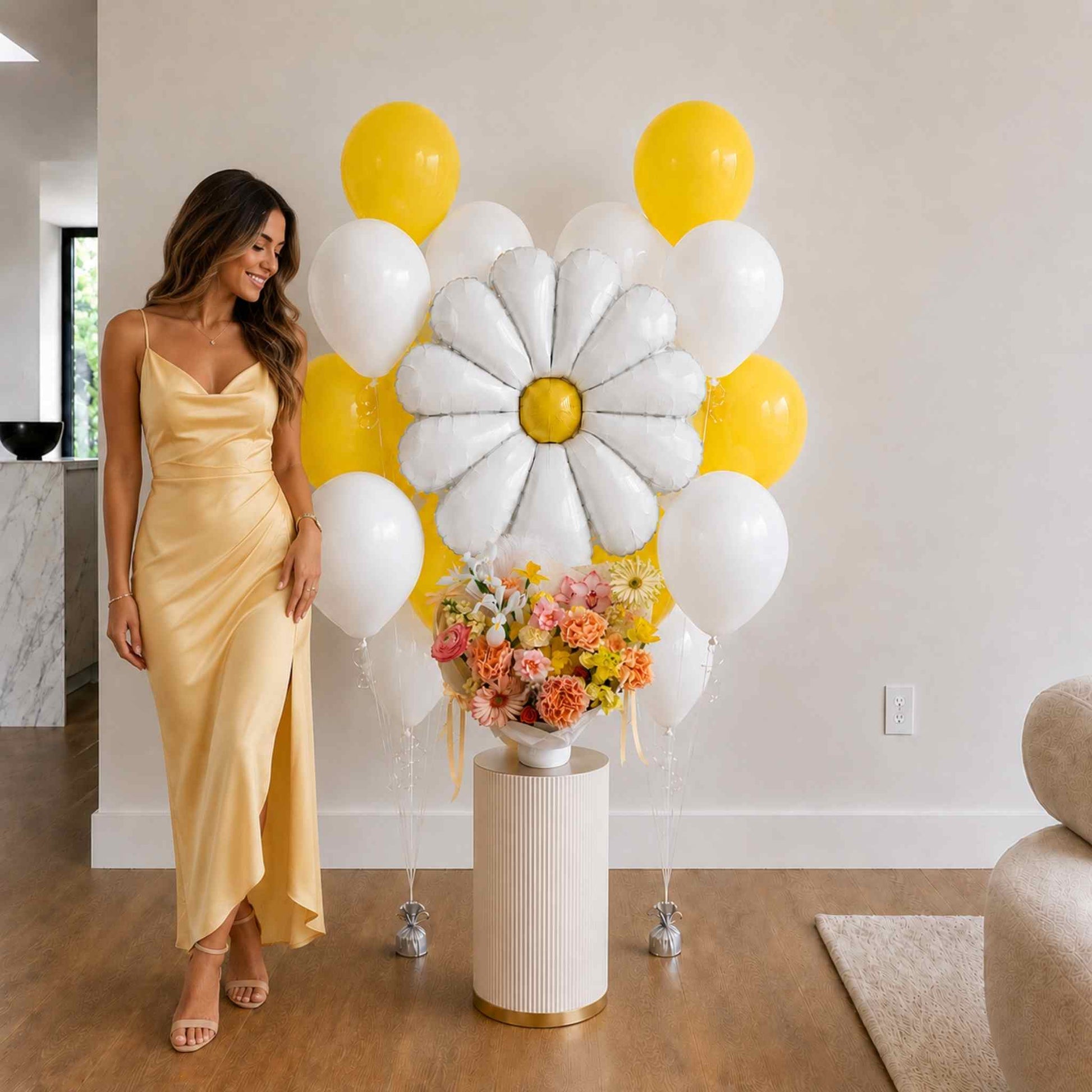 Woman in a yellow dress standing next to a floral arrangement and balloon arch in a room.