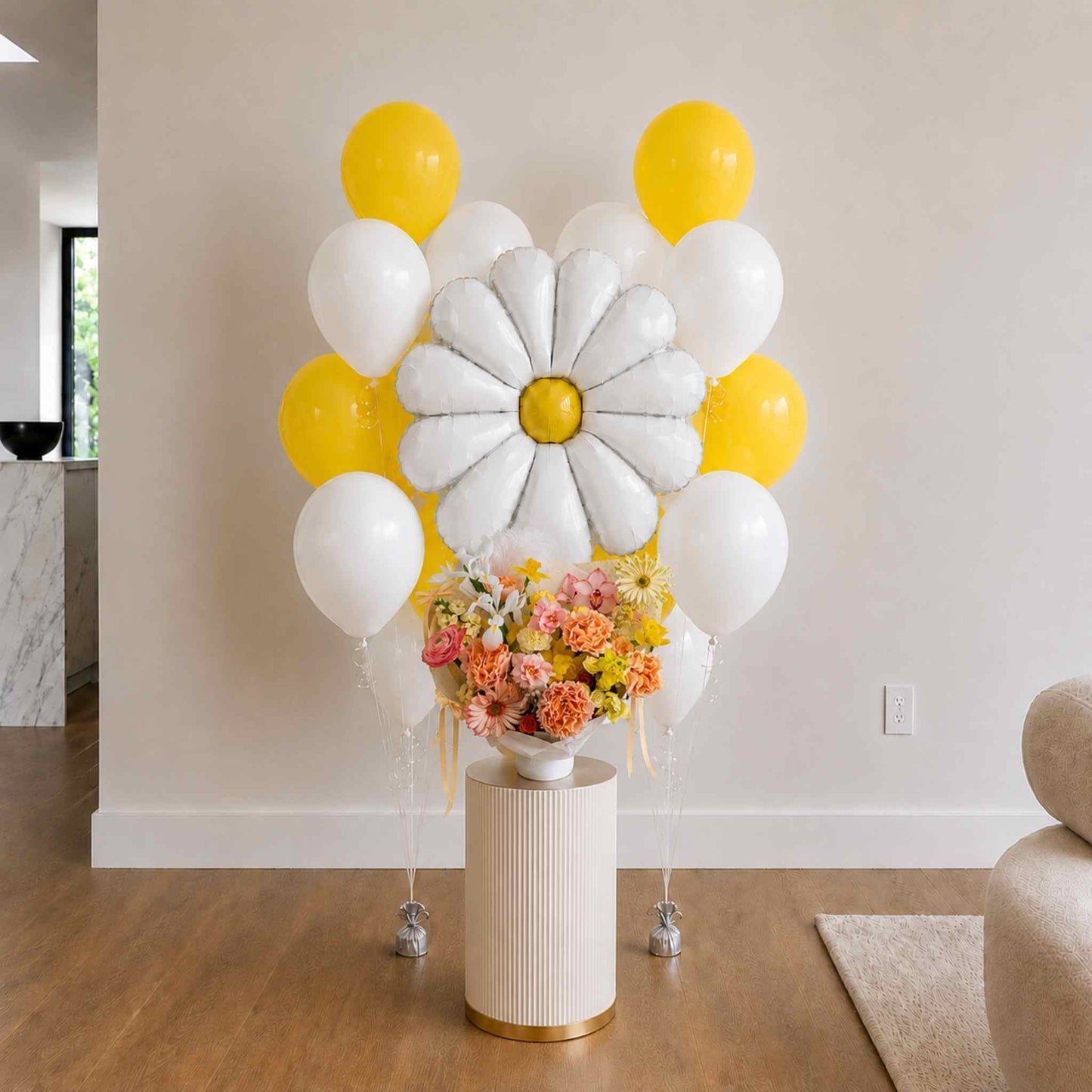 Balloon arch with white and yellow balloons and a flower arrangement on a small table.