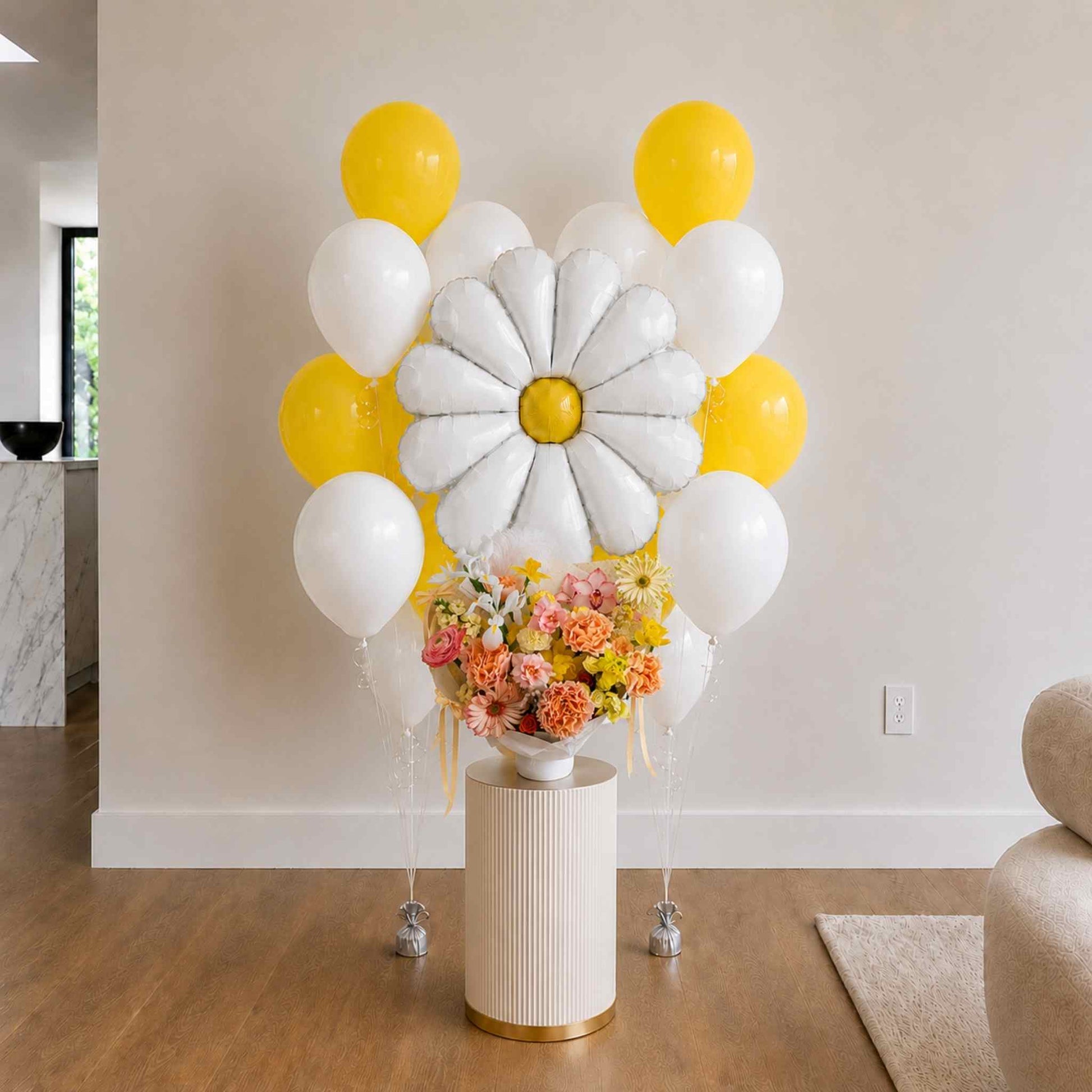 Balloon arch with white and yellow balloons and a flower arrangement on a small table.
