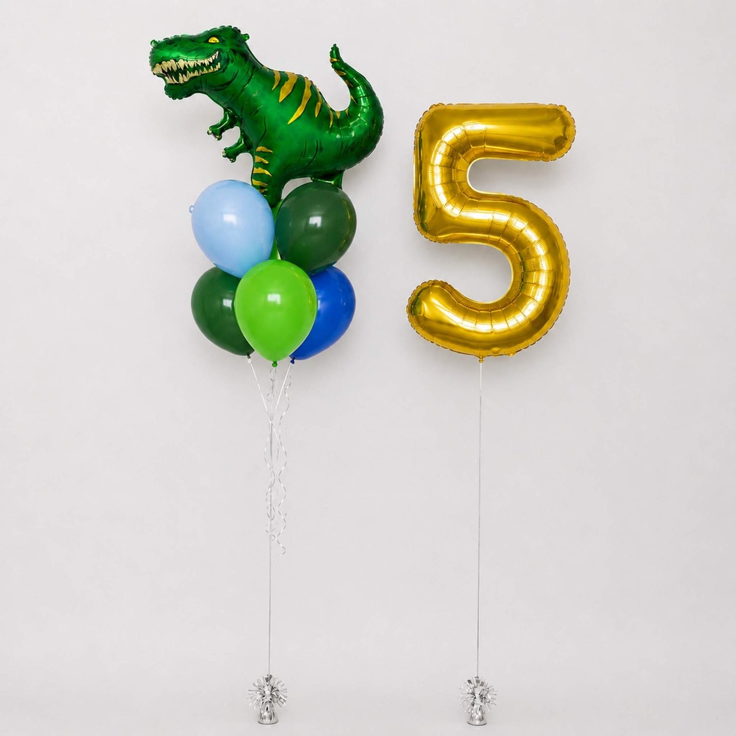 A set of party balloons including a metallic green dinosaur foil balloon, a large metallic gold number 5 foil balloon, and a cluster of smaller balloons in green, blue, and light blue, displayed against a plain light gray background.