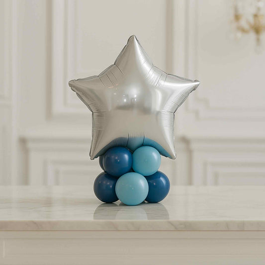 Silver star-shaped balloon with blue and light blue spherical balloons on a marble surface.