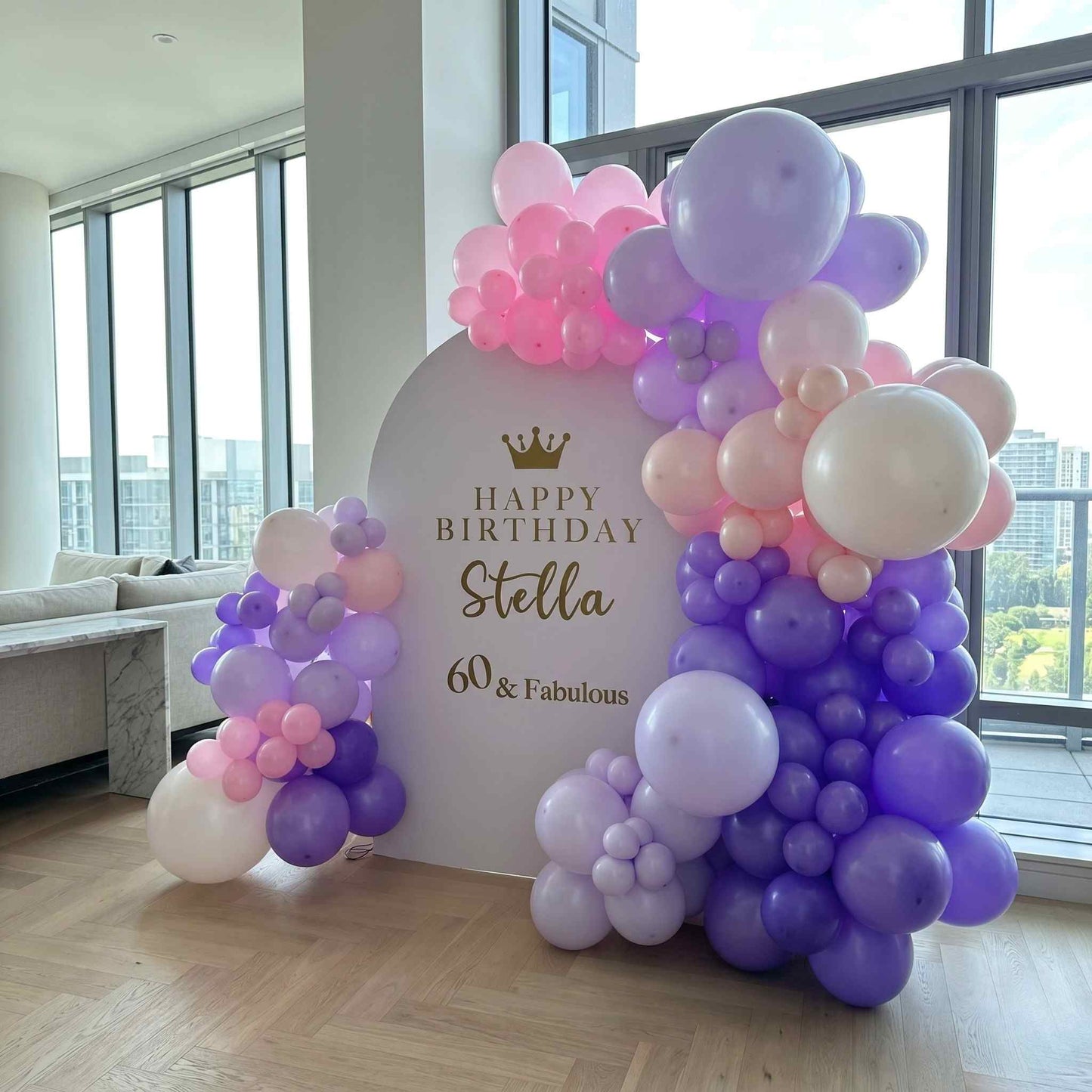 Balloon arch with 'Happy Birthday Stella 60 & Fabulous' sign in a room with large windows.
