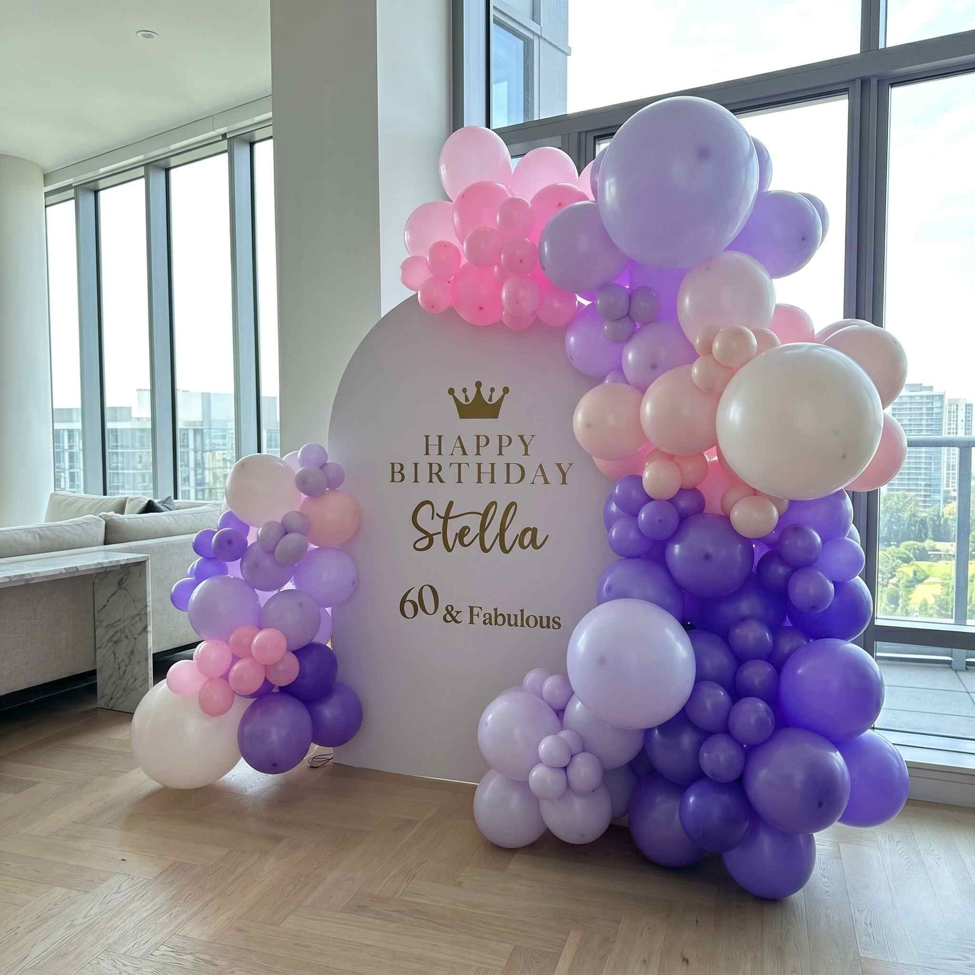Balloon arch with 'Happy Birthday Stella 60 & Fabulous' sign in a room with large windows.
