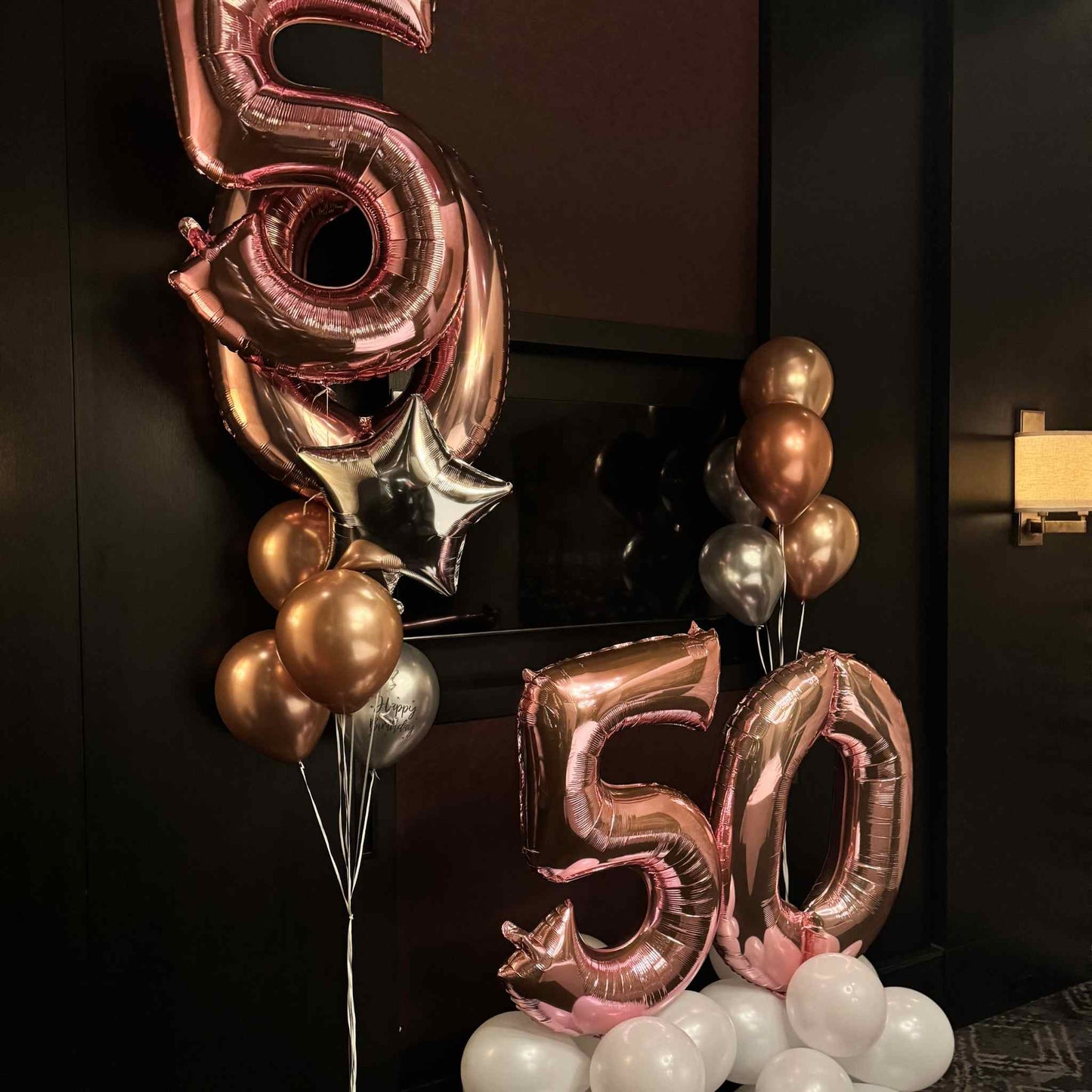 Rose gold '50' balloons with other balloons against a dark background