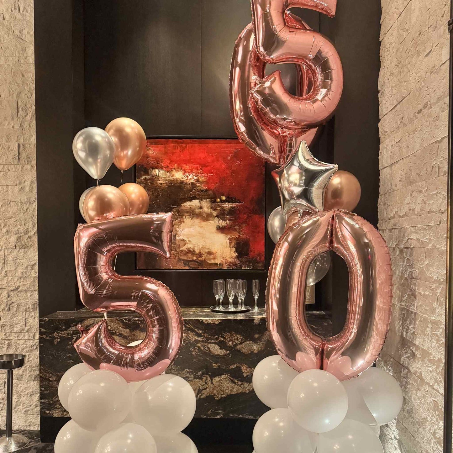 Rose gold '56' balloons with white balloons against a dark wall with abstract art.