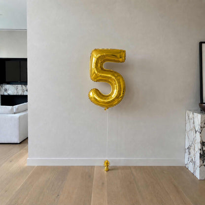 Gold number 5 balloon against a white wall in a room with a couch and fireplace.