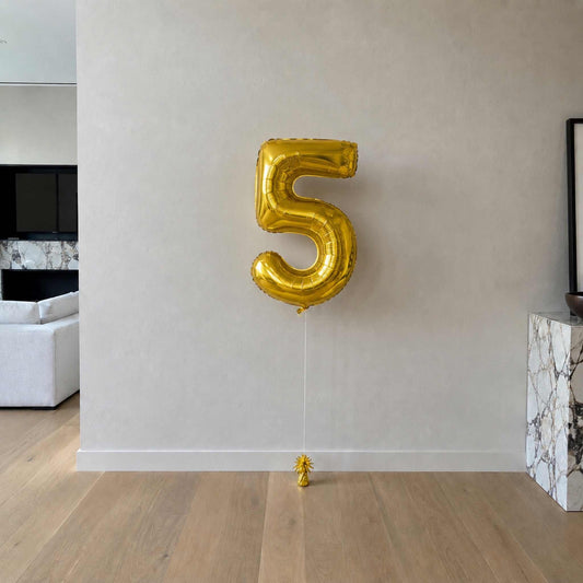 Gold number 5 balloon against a white wall in a room with a couch and fireplace.