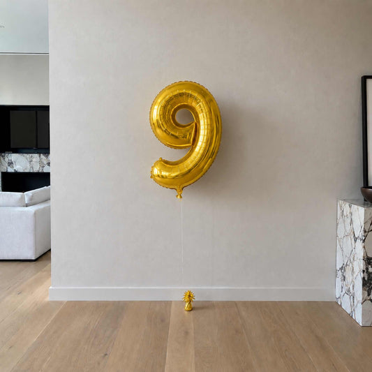 Gold number 9 balloon against a plain wall in a room with a couch and coffee table.