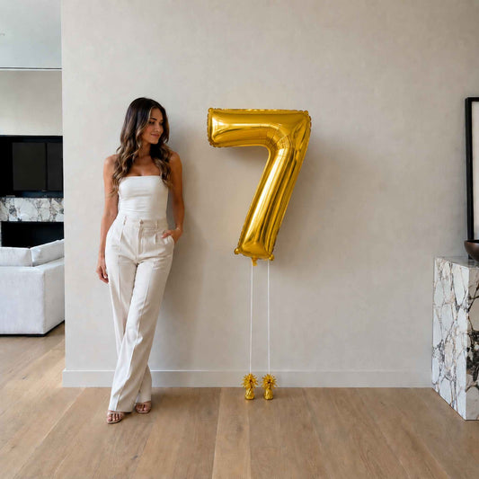 Woman standing next to a large gold number 7 balloon in a modern living room.