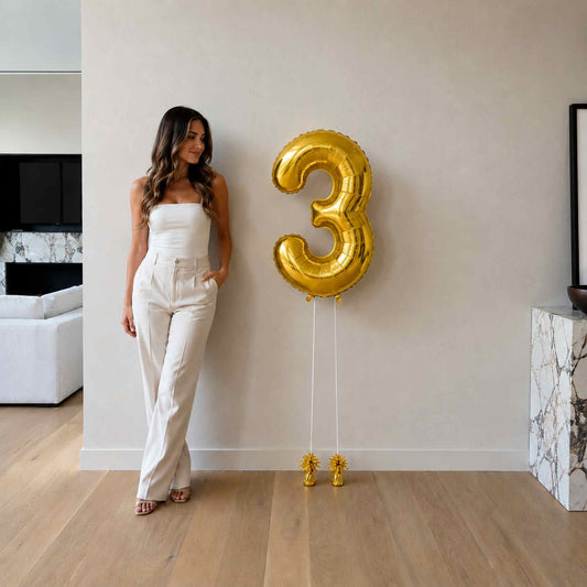 Woman standing next to a large gold number three balloon in a modern living room.