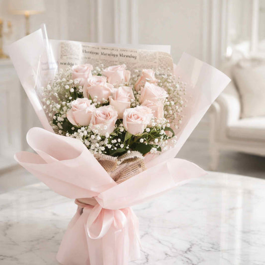 Bouquet of pink roses with baby's breath wrapped in newspaper and pink ribbon on a marble surface.