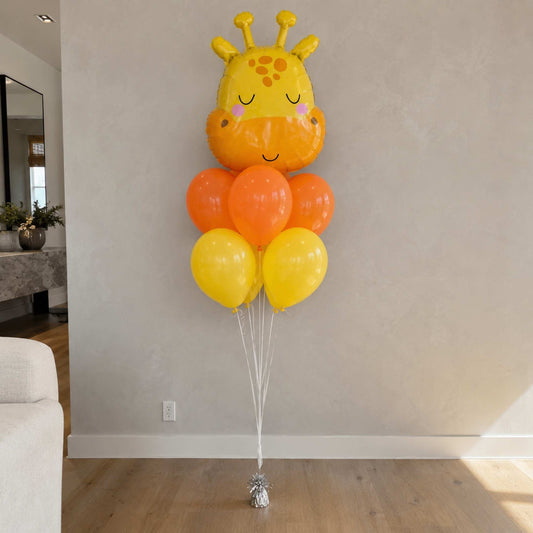 Giraffe-shaped balloon with orange and yellow balloons against a plain wall.