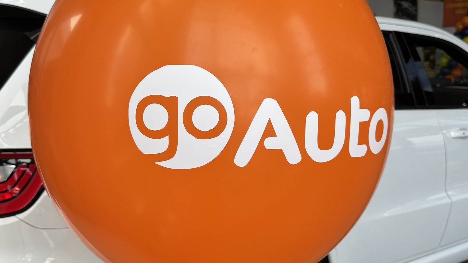 Orange balloon with 'goAuto' logo in front of a white car