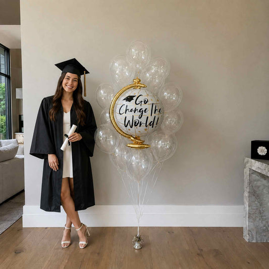 Graduate in cap and gown standing next to a large balloon with 'Go Change The World' text in a home setting.