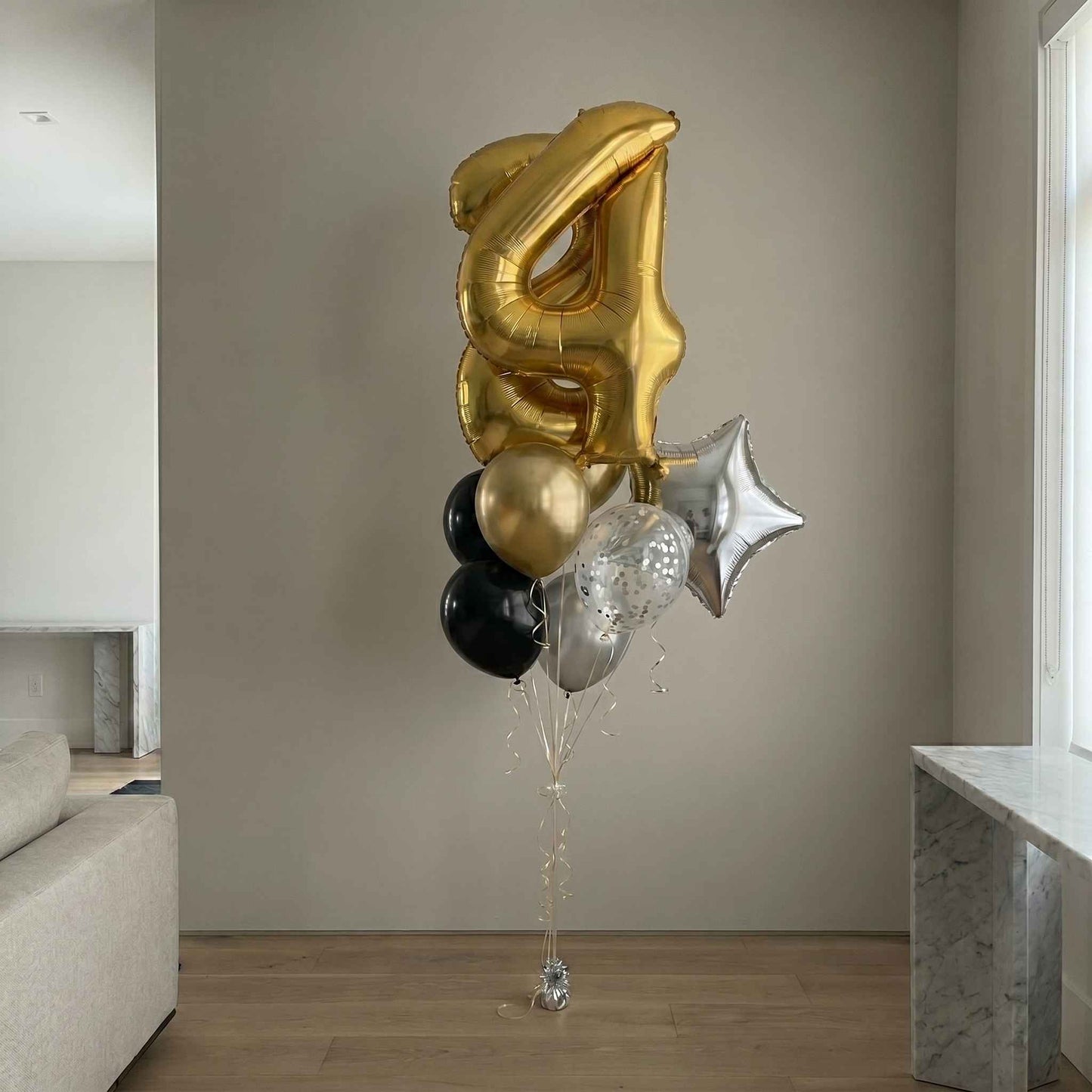 Gold, black, and silver balloons shaped like the number 4 in a living room.