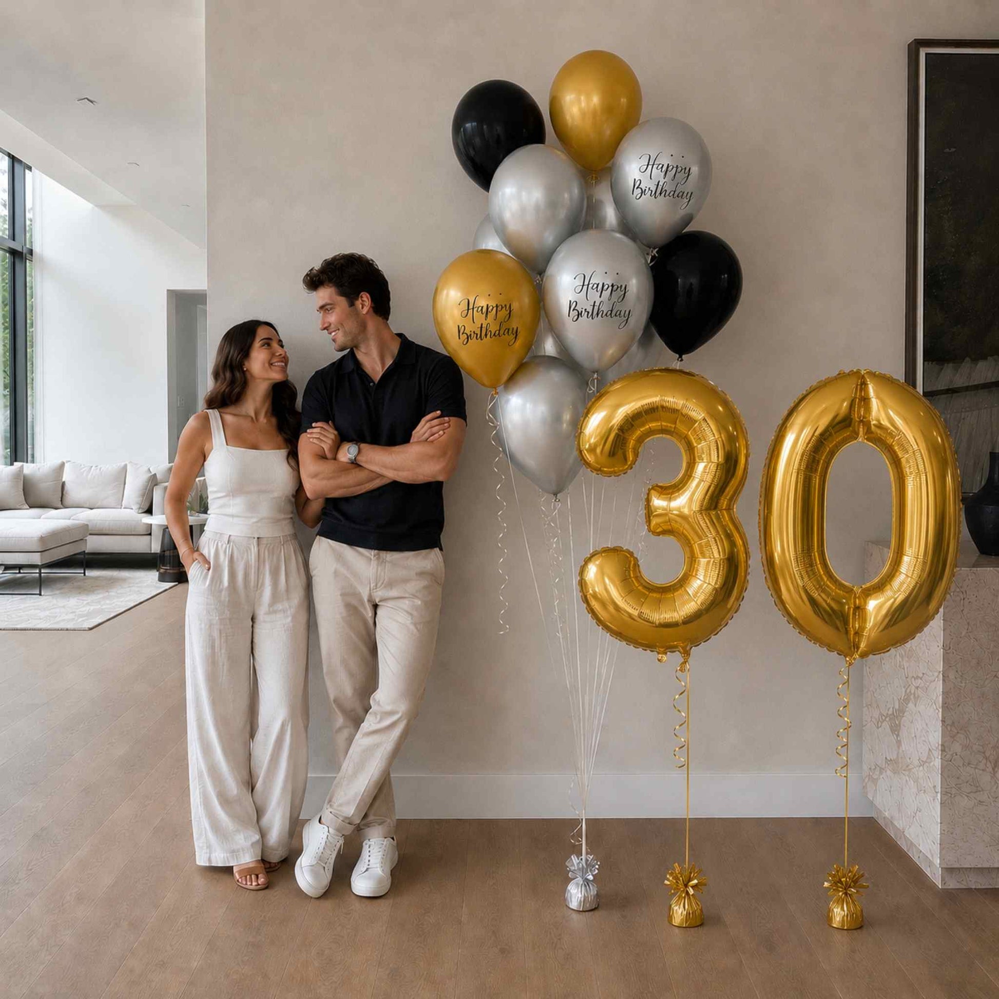 Couple standing next to large '30' gold balloons in a modern living room.
