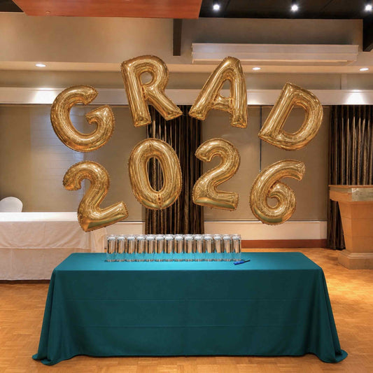 Gold 'GRAD 2026' balloons on a table with graduation caps in a formal setting.