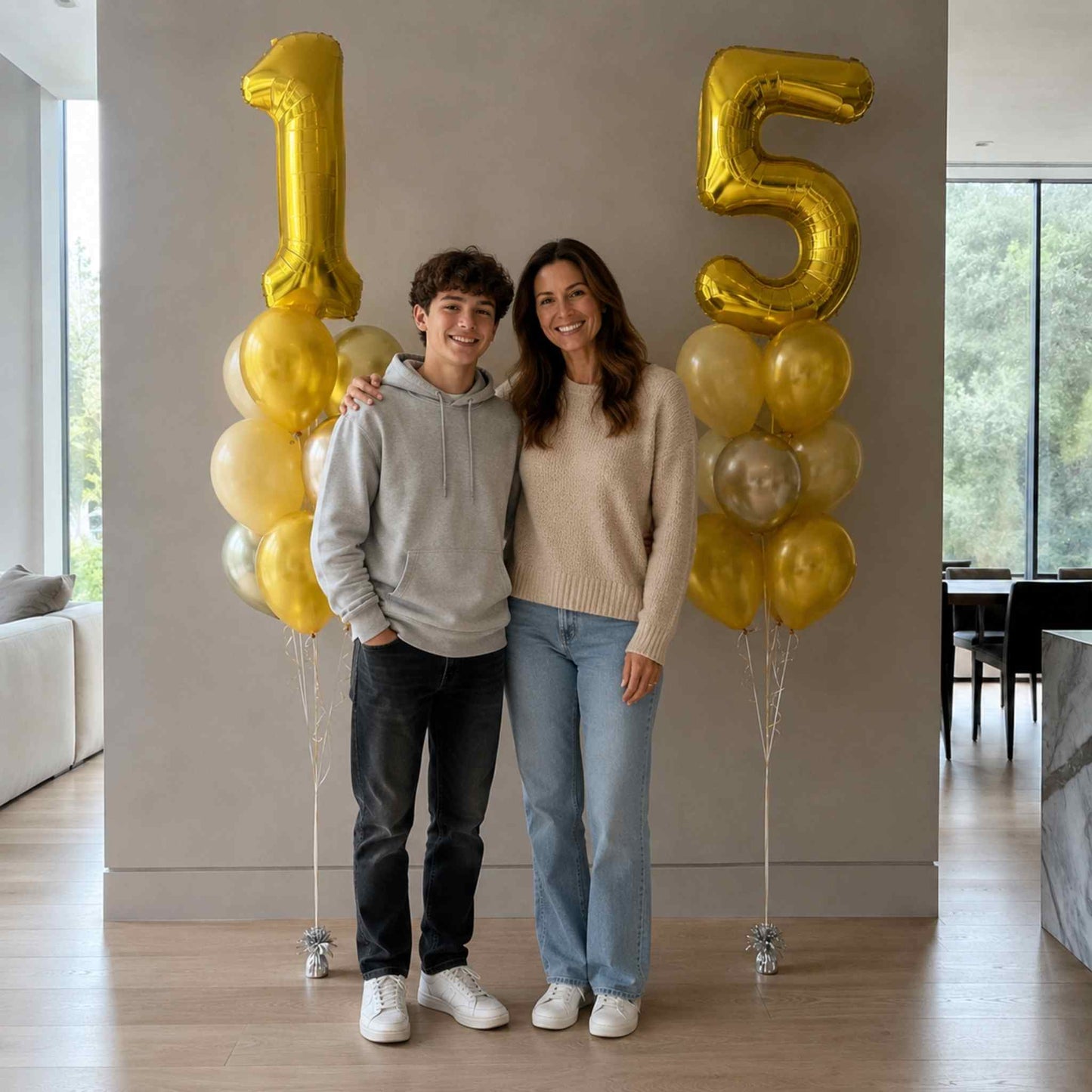 Two people standing in a room with gold and yellow balloons shaped like the number 15.