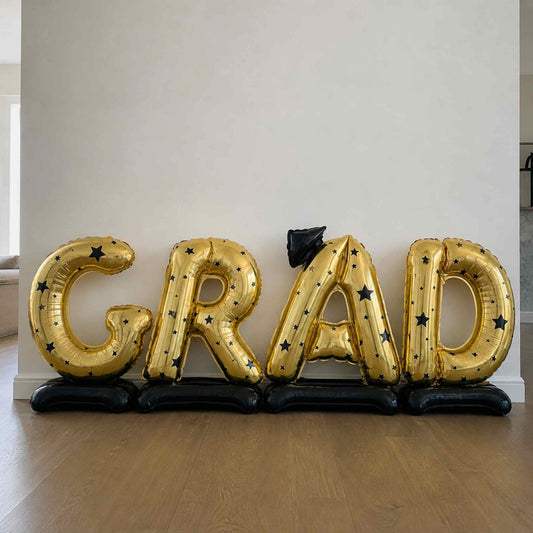 Gold 'GRAD' balloons on a wooden floor against a white wall