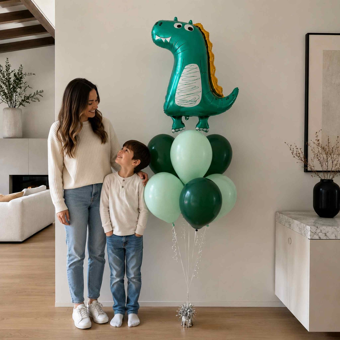 Woman and child standing next to a dinosaur-shaped balloon in a living room.