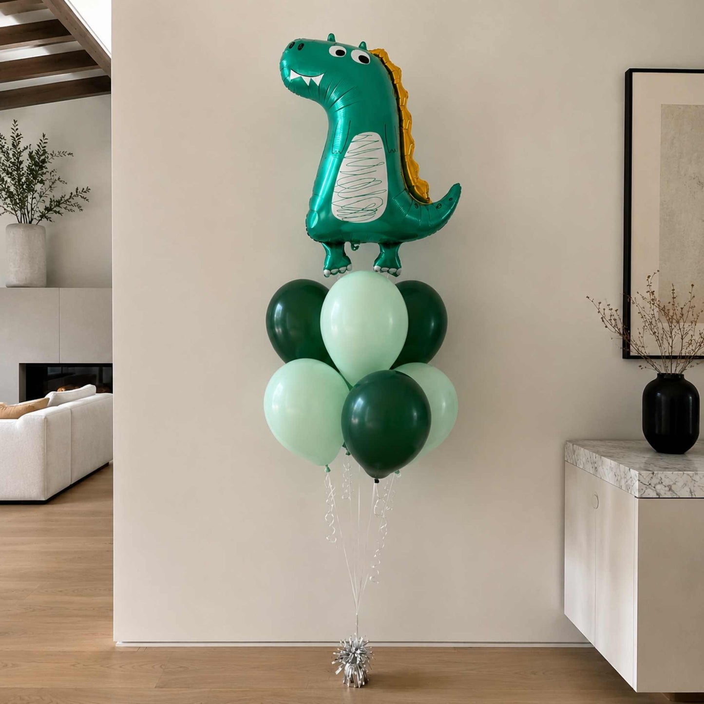 Dinosaur-shaped balloon with green and light green balloons in a living room setting.
