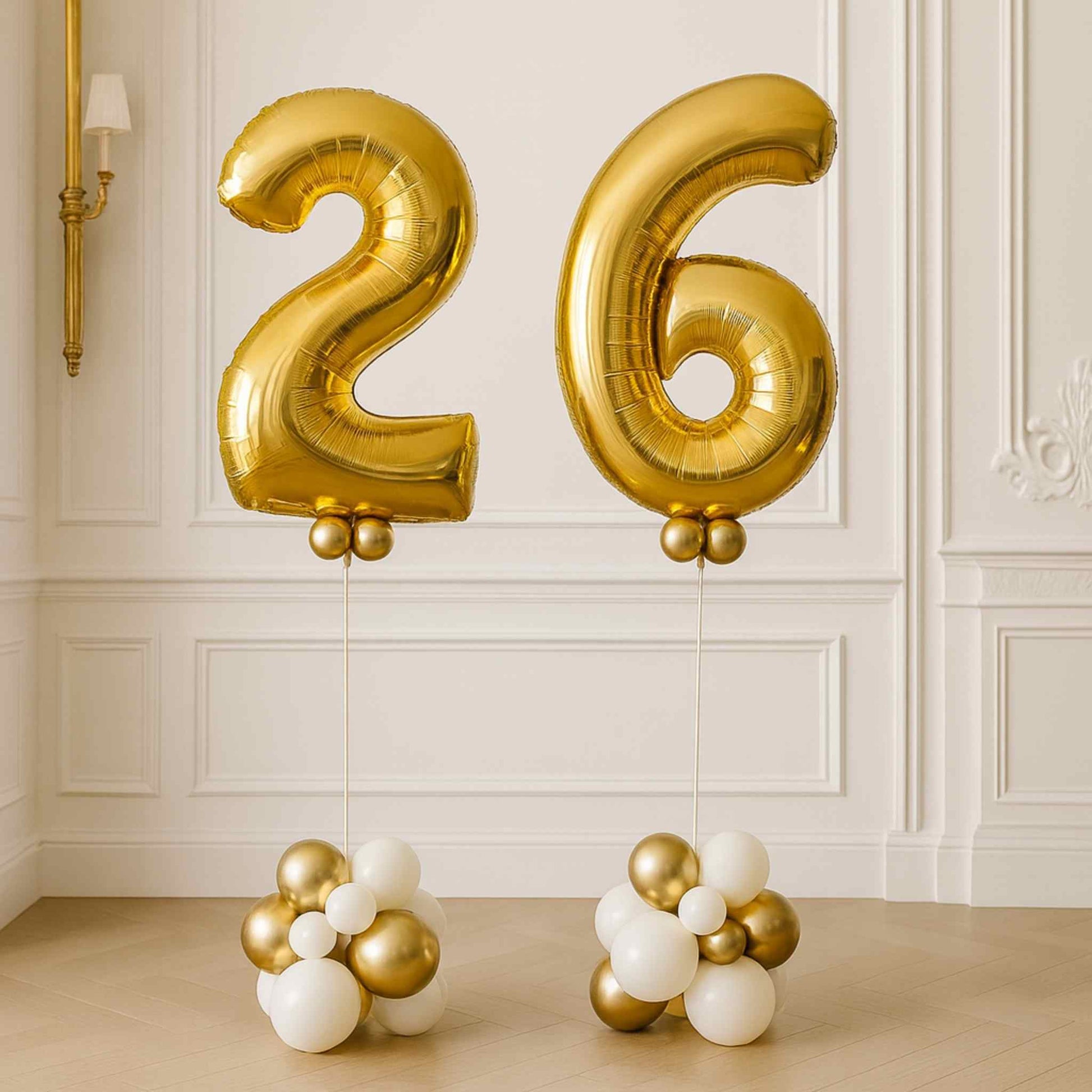 Gold helium number balloons “2” and “6” standing on white and gold balloon bases in an elegant white room.