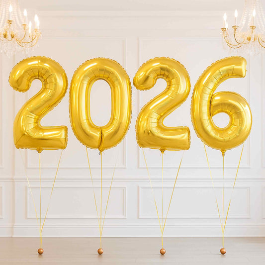 Gold '2026' balloons against a white wall with chandeliers.