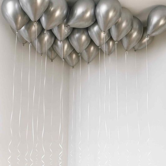 Silver balloons with strings against a white wall