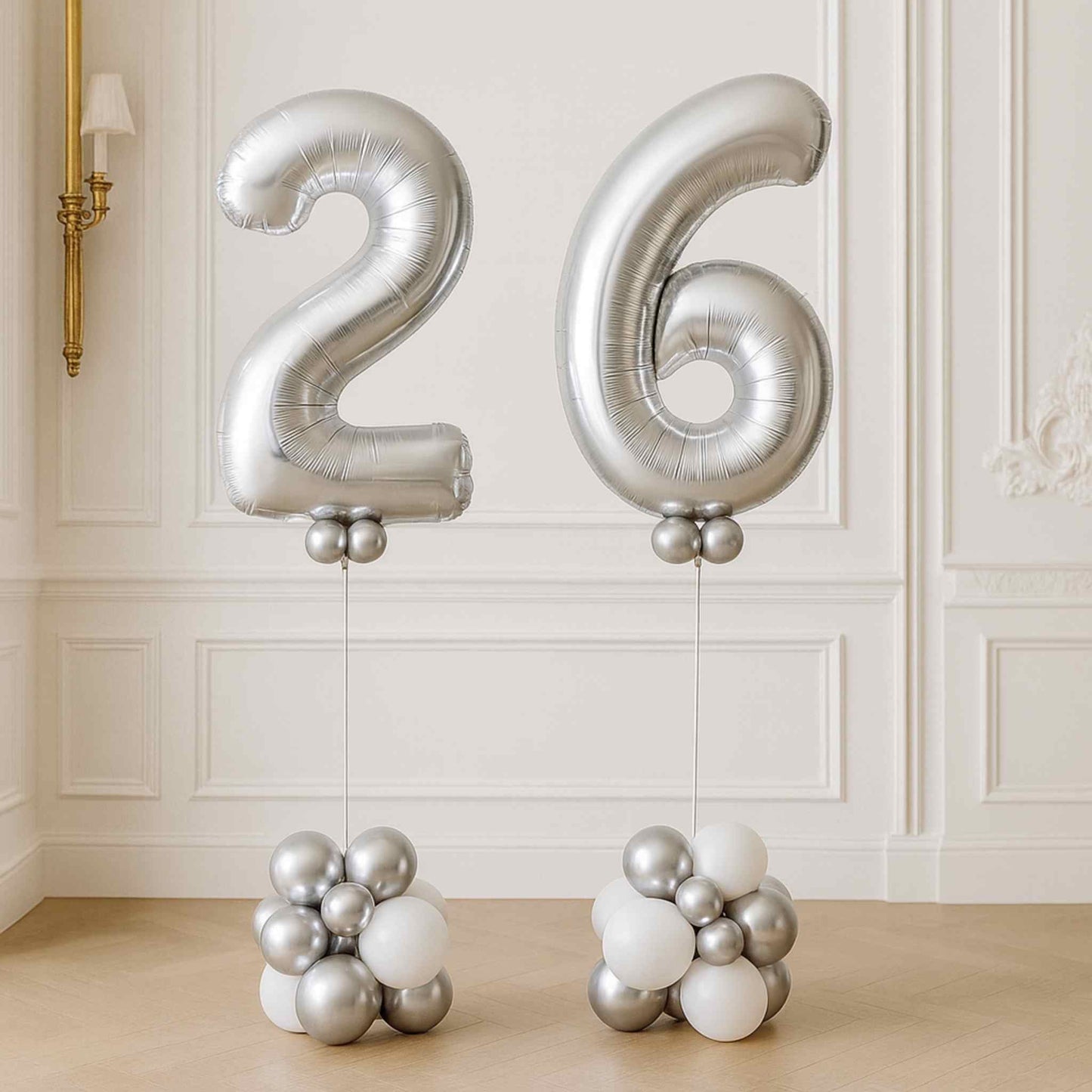 Silver helium number balloons “2” and “6” displayed on white and silver balloon bases in an elegant white room.