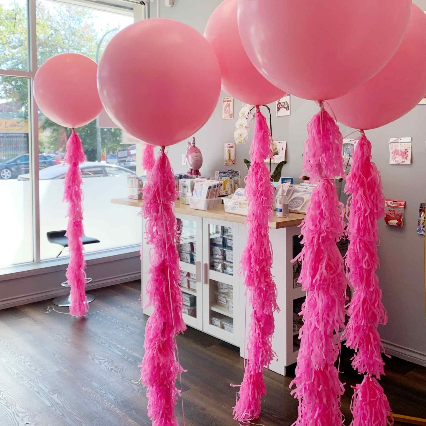 Pink balloons with tassels in a room with a window and furniture.