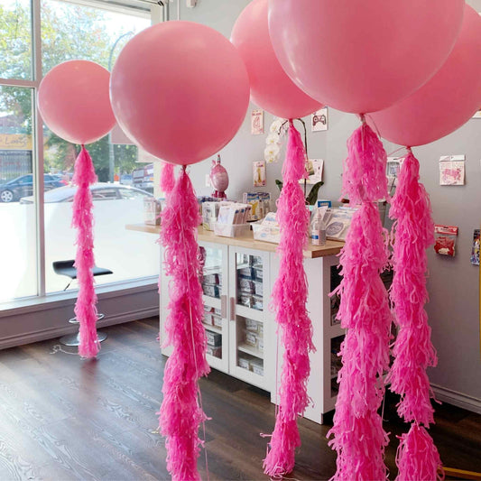 Pink balloons with tassels in a room with a window and furniture.