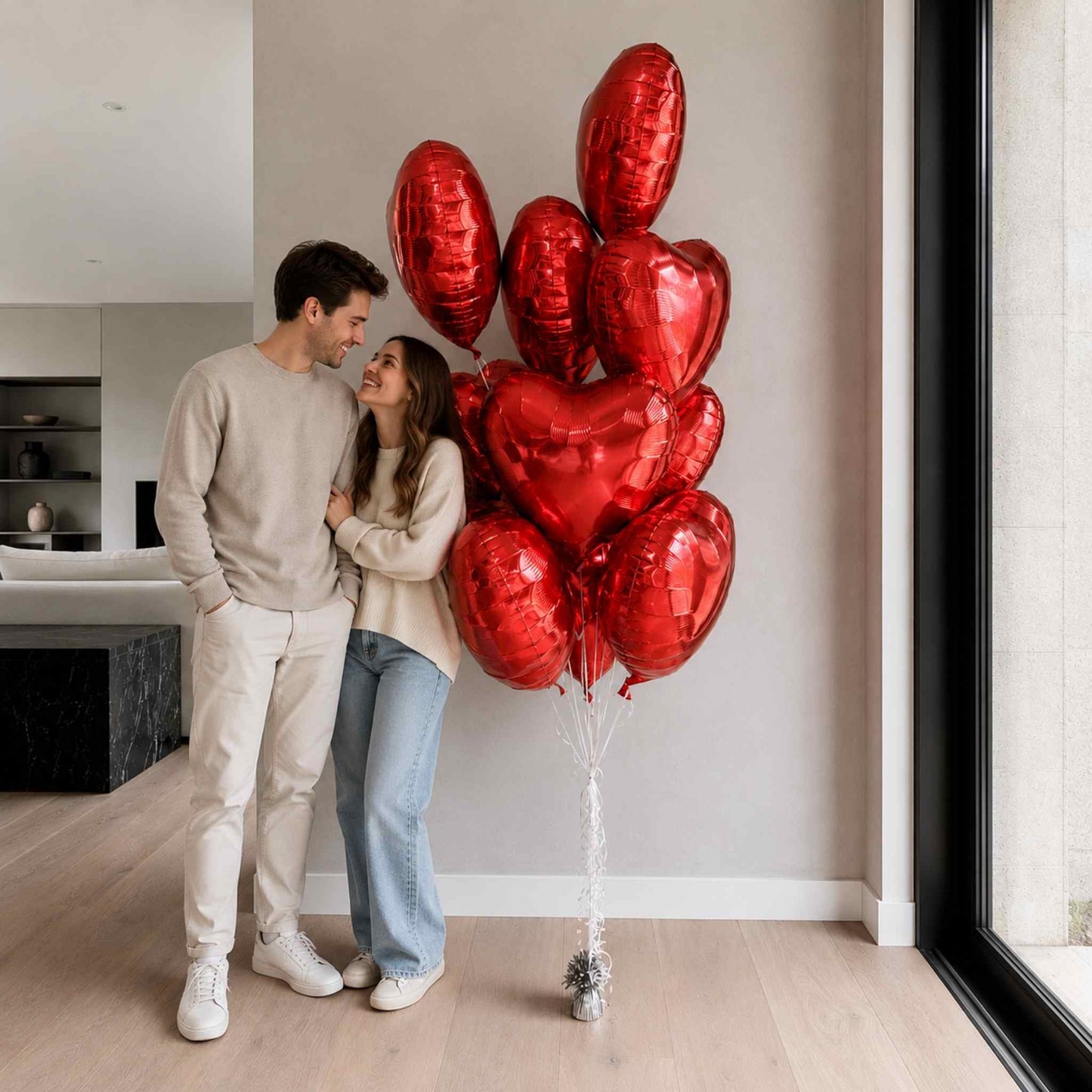 Couple standing in a modern living room with red heart-shaped balloons.