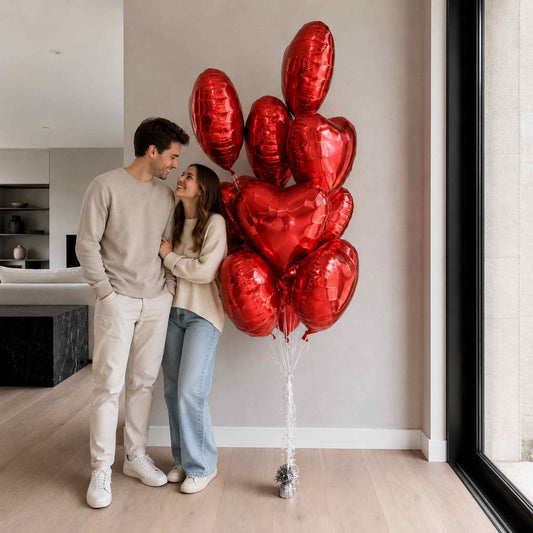 Couple standing in a modern living room with red heart-shaped balloons.